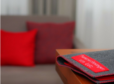 Dark guest folder with red label “Ferienwohnungen von Lutz” on table, red cushions in background.