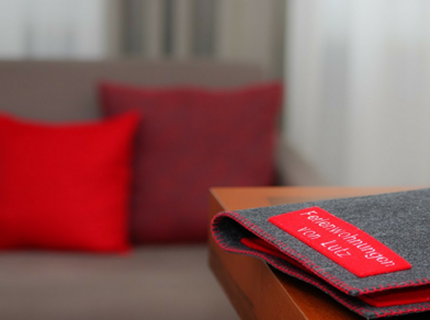 Dark guest folder with red label “Ferienwohnungen von Lutz” on table, red cushions in background.