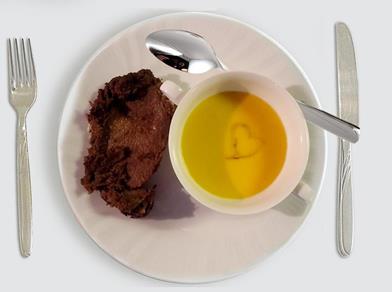 Teller mit Kürbissuppe in Tasse und Bratenstück, Suppenoberfläche zeigt ein Herzmotiv aus Sahne.