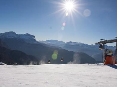 Paesaggio innevato con funivia e sole splendente, vista limpida sulle Dolomiti.
