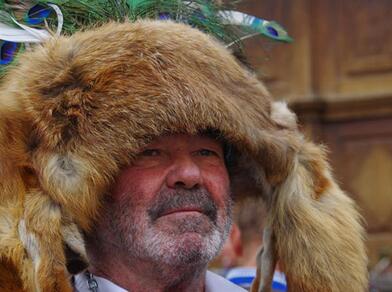 An older man wearing a traditional fur hat adorned with peacock feathers