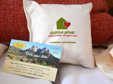 Stone pine pillow with “südtirol privat” logo and Villa Erna business card in front of red cushion.