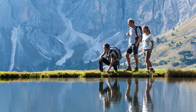 Three hikers near a lake; in the background the Dolomites