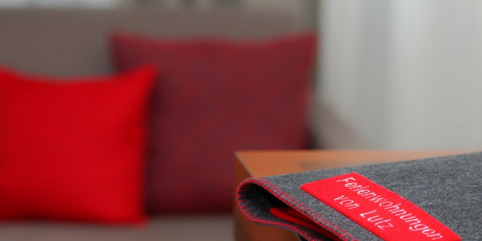 Dark guest folder with red label “Ferienwohnungen von Lutz” on table, red cushions in background.