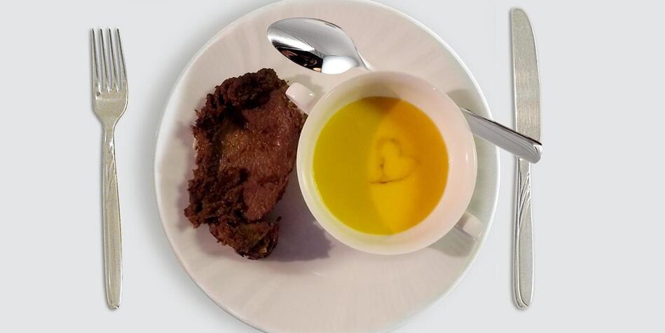 Plate with pumpkin soup in a cup and a slice of roast; a heart shape decorates the soup’s surface.