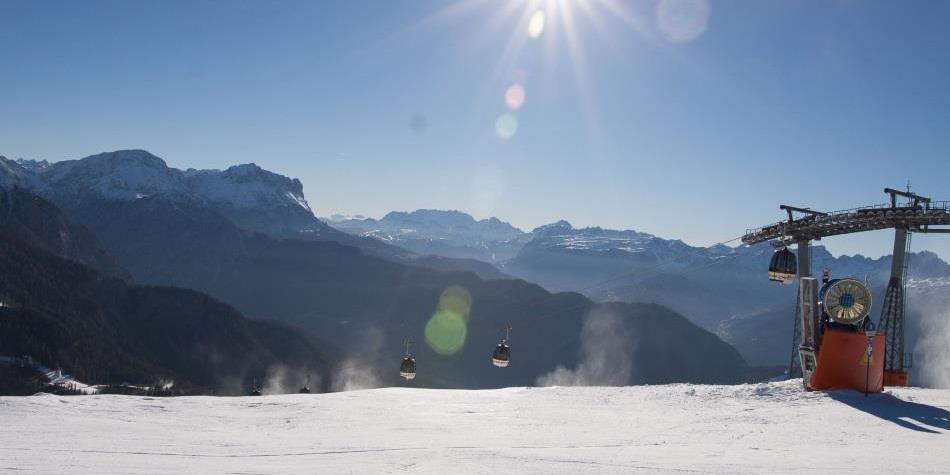 Paesaggio innevato con funivia e sole splendente, vista limpida sulle Dolomiti.