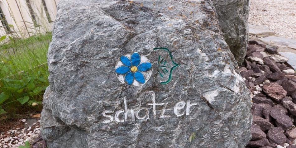 Großer grauer Stein mit einer gemalten blauen Blume und dem Wort „schatzer“