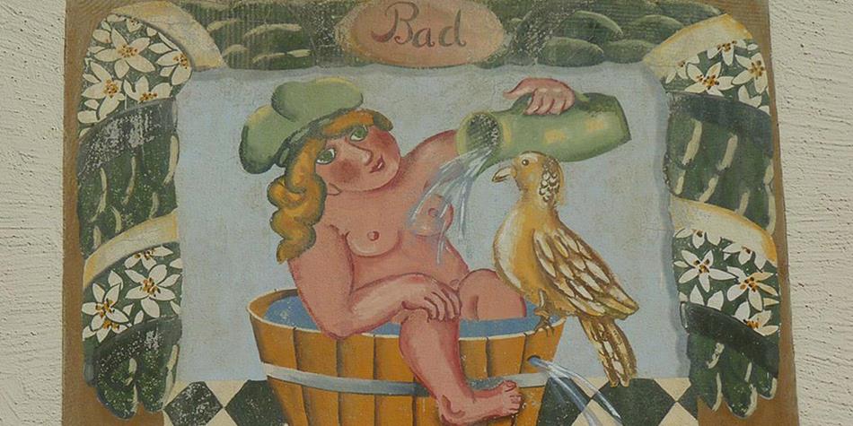Traditional mural painting showing a child in a wooden tub washing and pouring water for a bird; decorated with floral patterns and the word “Bad” (bath).