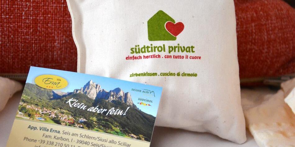 Stone pine pillow with “südtirol privat” logo and Villa Erna business card in front of red cushion.