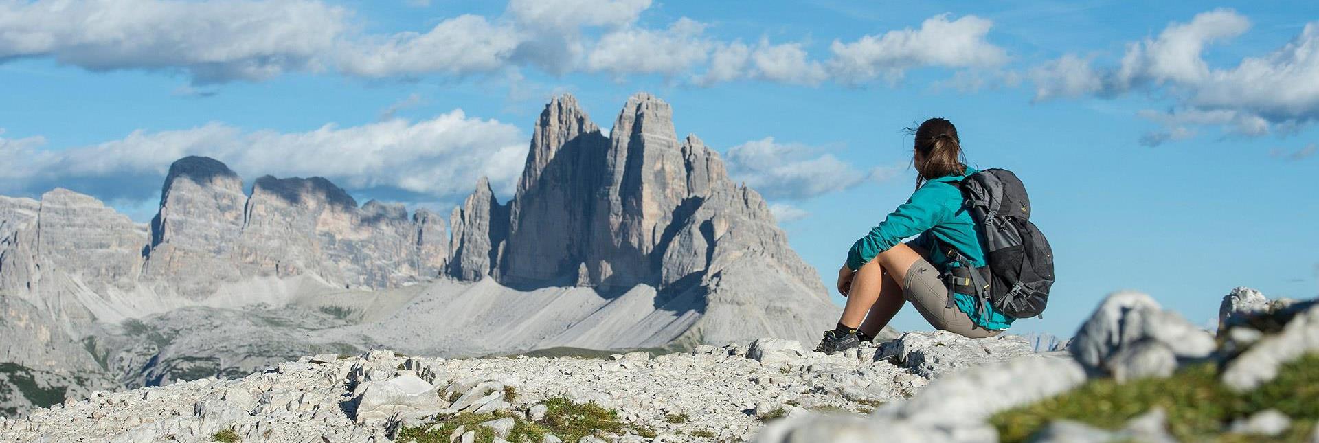 A female hiker is sitting on a rock and looking at the Three Peaks